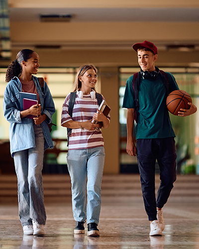 photo of three kids walking down a school hallway with books and a basketball and smiling