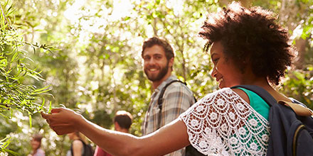 A woman reaches out to touch the leaves of a tree while smiling